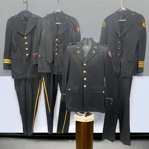 May include: Four black military dress uniforms with gold buttons and trim. The uniforms have different styles and details, including a purple stripe on one of the jackets.
