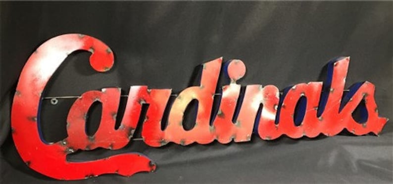 May include: Red metal sign with the word "Cardinals" in a stylized font. The sign has a distressed look, with a blue outline around the letters.