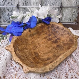 May include: A large, rustic wooden bowl with a natural brown finish. The bowl has a unique, hand-carved design and is perfect for serving or displaying items.