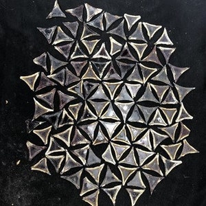 May include: A close-up of a black surface with a pattern of clear, triangular glass pieces. The pieces are arranged in a geometric pattern, creating a mosaic effect.