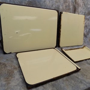 Puede incluir: Cuatro tapas de cocina de esmalte blanco roto con ribetes negros. Las tapas son rectangulares y tienen un borde ligeramente redondeado.