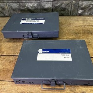 May include: Two gray metal toolboxes with labels. The top toolbox has a label that reads "AMP" and "MS 252 Repair Kit". The bottom toolbox has a label that reads "AMP" and "PIDG Kit". Both toolboxes have a handle and a latch.