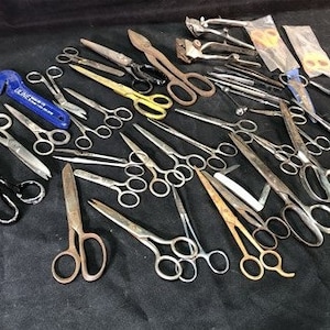 May include: A collection of vintage scissors, including a pair of yellow-handled shears, a pair of blue-handled shears, and a pair of silver-handled shears. The scissors are arranged on a black surface.