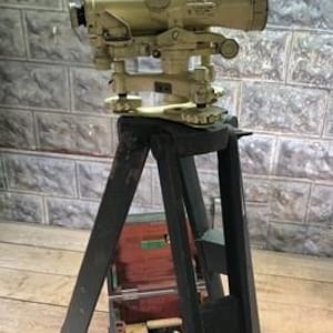 May include: A vintage brass theodolite surveying instrument on a wooden tripod with a wooden box. The theodolite has a telescope and a graduated circle.