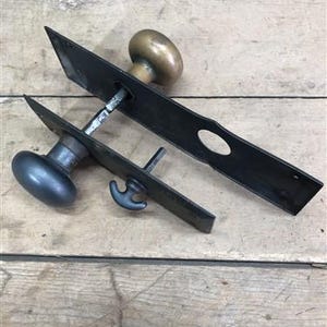 May include: Antique door hardware with a black metal plate and two brass knobs. The plate has a keyhole and a latch. The knobs are round and have a smooth finish.