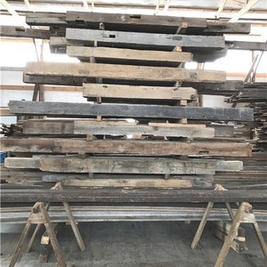 Puede incluir: Una pila de vigas de madera recuperada, algunas con agujeros y nudos, listas para usar en un proyecto de bricolaje.