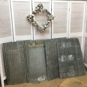 May include: Four pieces of corrugated metal sheeting, weathered and rusty, with a light gray color. The sheeting is arranged in a row on a wooden floor.
