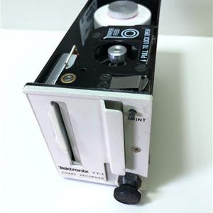 May include: A Tektronix YT-1 chart recorder, a vintage electronic device, is shown. The device has a white and black casing with a paper feed mechanism and a black knob. The text "PULL TO LOCK OPEN" is visible on the device.