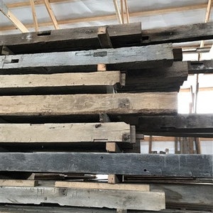 Puede incluir: Una pila de vigas de madera recuperada, algunas con nudos e imperfecciones visibles, en un entorno de granero r&uacute;stico.