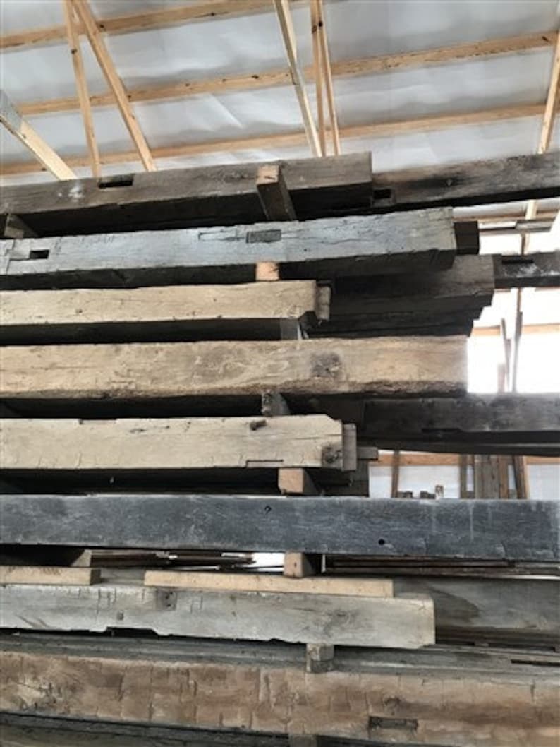 Puede incluir: Una pila de vigas de madera recuperada, algunas con nudos e imperfecciones visibles, en un entorno de granero r&uacute;stico.