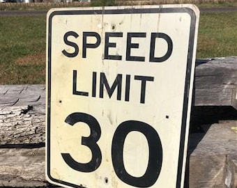 Peut inclure: Un panneau de limitation de vitesse rectangulaire et usé, indiquant "SPEED LIMIT 30" en lettres noires grasses. Le panneau a un fond crème et un bord noir. Le chiffre 30 est bien visible. Le panneau est monté sur une surface en bois.