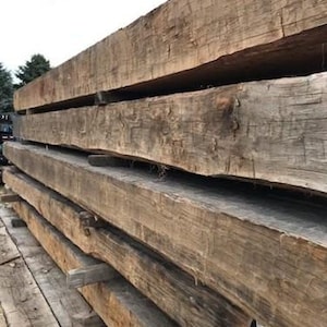 May include: A stack of four reclaimed wood beams, showing the natural grain and texture of the wood. The beams are weathered and have a rustic appearance.