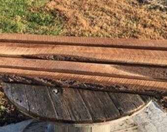 May include: Four pieces of rough-cut, natural wood planks with a rustic, weathered look. The planks are stacked on top of each other and have a natural brown color.