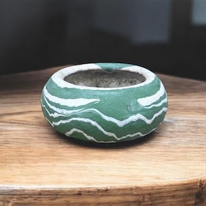 Könnte beinhalten: Eine kleine, runde, grüne Keramikschale mit weißen wellenartigen Mustern. Der Innenraum ist neutralgrau. Die Schale steht auf einer Holzoberfläche. Diese dekorative Schale kann für kleine Pflanzen oder als dekoratives Element verwendet werden.