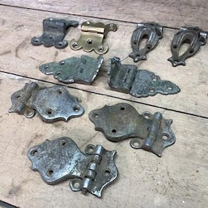 May include: A collection of antique hinges in a variety of styles and finishes, including brass, iron, and steel. Some hinges feature ornate designs, while others are more plain. These hinges would be a great addition to any vintage or antique project.
