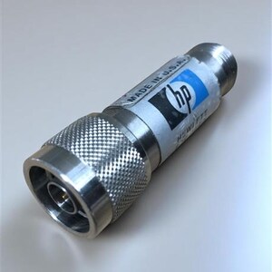 Può includere: Un connettore color argento con un'impugnatura strutturata e un corpo cilindrico liscio. Il connettore ha un'etichetta con la scritta "MADE IN U.S.A." e il logo "hp" in blu e nero. È visibile anche il marchio "HEWLETT".
