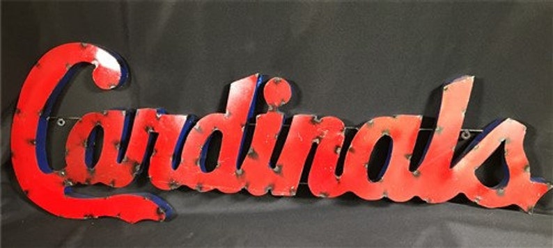 May include: Red metal sign with the word "Cardinals" in blue outlined letters. The sign has a distressed, vintage look.