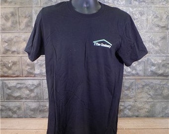 May include: Black t-shirt with a green and white logo that says "The Gallery" on the front.