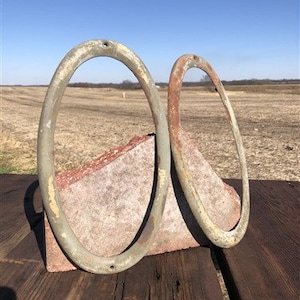 May include: Two antique metal oval rings with a weathered green and brown patina. The rings are sitting on a piece of broken brick.