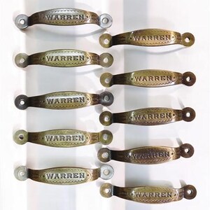 May include: Ten antique brass cabinet door pulls with the word "WARREN" engraved on each. The pulls have a decorative, scalloped edge.
