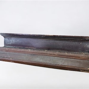 May include: A dark brown wooden cornice with a decorative molding. The cornice is made of multiple layers of wood and has a slightly weathered appearance.