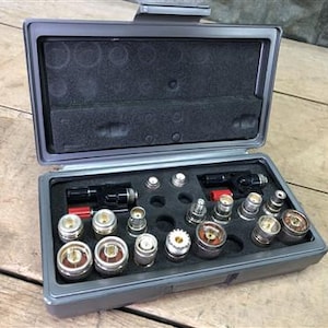 May include: An open gray toolbox with a variety of metal fittings and components. The interior is lined with black foam, and the tools are neatly arranged. The toolbox is on a wooden surface.