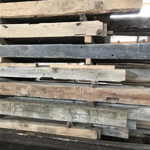 Puede incluir: Una pila de vigas de madera recuperada, algunas son de color marr&oacute;n oscuro, otras son de color marr&oacute;n claro y algunas son grises. Las vigas est&aacute;n apiladas en un orden aleatorio.