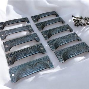 Peut inclure: Dix poignées de tiroir de style antique avec un motif floral décoratif. Les poignées sont en métal et ont une finition bleu foncé.