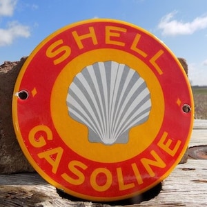 Könnte beinhalten: Ein rundes Metallschild mit den Worten "Shell Gasoline" und einem weißen Muschel-Logo in der Mitte, in rot und gelber Farbe.
