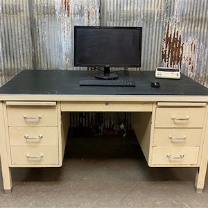 May include: A vintage metal desk with a black laminate top, three drawers on each side, and a black computer monitor on top.