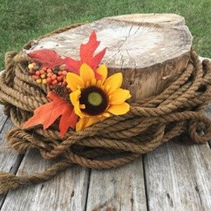 May include: A rustic wooden slice cake stand decorated with a sunflower, fall leaves, and brown rope.
