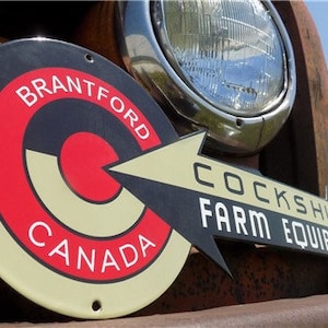 May include: A vintage metal sign with a red, white, and black target design. The sign reads "Brantford Canada" and "Cockshutt Farm Equipment".