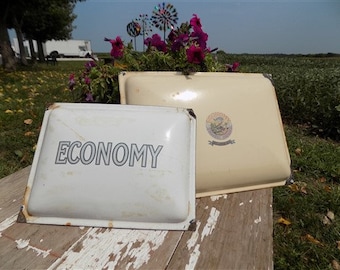 May include: Two vintage enamel signs, one white with the word "ECONOMY" in black lettering, and the other cream with a decorative design and a gold seal.