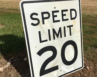 Peut inclure: Panneau de limitation de vitesse blanc avec du texte et des chiffres noirs. Le panneau indique "SPEED LIMIT 20".