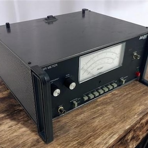 Puede incluir: Un medidor VR negro con un asa y un panel lateral de malla. El medidor tiene un indicador con una aguja y varias perillas y botones. El texto "VR METER" es visible en la parte frontal.