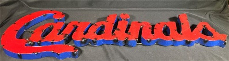 May include: Red and blue metal sign with the word "Cardinals" in raised letters. The letters have a distressed look, with some of the paint chipped away.