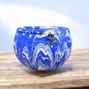Könnte beinhalten: Ein runder, blau-weißer Keramik-Pflanztopf mit Marmormuster. Der Pflanztopf hat eine strukturierte Oberfläche und ein einzigartiges, gewirbeltes Muster. Die Farbpalette umfasst Blau- und Weißtöne und schafft ein dekoratives Stück.