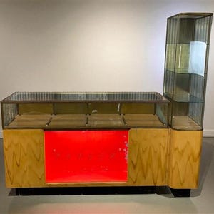 May include: A vintage display case with a glass top and sides, featuring a wooden base and a red panel. The display case has a tall, vertical glass section on the right side. The word "PARKER" is visible on the red panel.