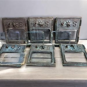 Pode incluir: Seis capas de ranhura de correio antigas de bronze com inserções de vidro. Cada capa apresenta um desenho floral acima da letra "S". O bronze tem um aspeto envelhecido e desgastado, com toques de verdete. As inserções de vidro são claras e retangulares.