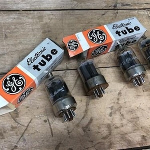 May include: A collection of vintage electronic tubes with clear glass and metal bases, presented with their original orange and white boxes. The boxes are labelled "Electronic tube" and feature a black and white logo.
