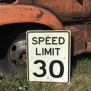 May include: A white and black speed limit sign with the text "SPEED LIMIT 30" on a rusty truck.