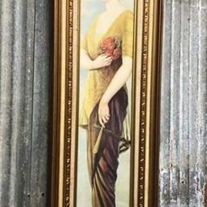 May include: A tall, rectangular framed print featuring a portrait of a person with short dark hair wearing a headband, a yellow top, and a long dark skirt. The person holds a bouquet of red flowers and a fan, encased in a gold-toned frame.