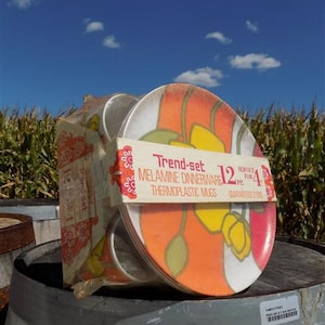 May include: A vintage Trend-set melamine dinnerware set, including plates and thermoplastic mugs. The plates feature a colorful floral design with orange, yellow, and green accents. The set is packaged and includes the text "Trend-set MELAMINE DINNERWARE 12 pc. SERVICE FOR 4 GUARANTEED 2 YRS."