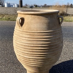 May include: A large, terracotta planter with a ribbed design and two handles. The planter is made of a rough, textured material and has a natural, earthy color.