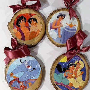 Pode incluir: Quatro enfeites de madeira redondos com imagens do filme Aladdin. Cada enfeite é uma fatia de madeira com uma imagem impressa e uma fita bordô para pendurar. As imagens mostram Aladdin, Jasmine e o Gênio.