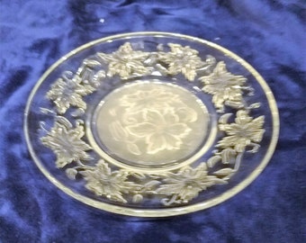 May include: A clear glass plate with a floral design etched into the surface. The design features a repeating pattern of leaves and flowers.