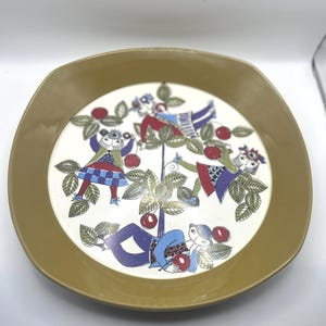 May include: A vintage ceramic plate with a whimsical design. The plate features a cream-colored center with a colorful illustration of figures picking cherries from a tree. The rim is a solid olive green color. A unique piece for display or dining.