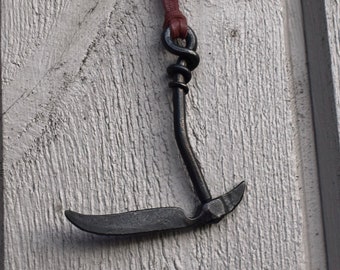 May include: A black metal hook with a brown leather cord hanging on a white wooden wall.