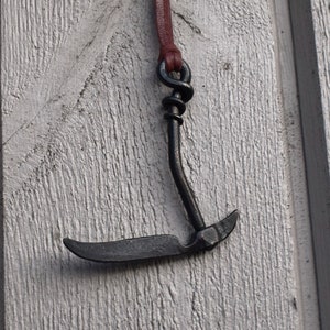 May include: A black metal hook with a brown leather cord hanging on a white wooden wall.