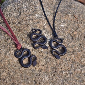 May include: Three black snake pendant necklaces on a rock background. The necklaces are made of wood and have a simple, elegant design. The pendants are all different sizes and shapes.
